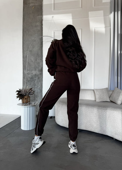 Person wearing a dark brown tracksuit in a modern room with a sofa and decorative items.