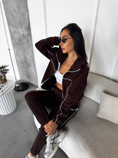 Woman in a brown tracksuit sitting on a couch in a modern living room.