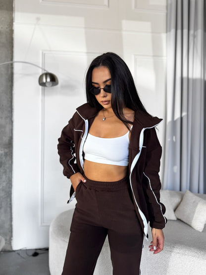 Woman wearing a brown jacket and pants with a white top in a modern room.