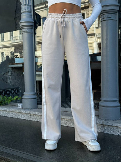 Person wearing light gray sweatpants with a white stripe outdoors.