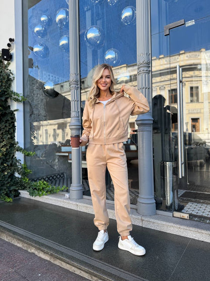 Woman in beige tracksuit standing in front of a glass building