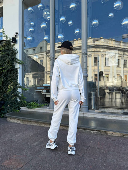 Person wearing a white tracksuit standing in front of a reflective building facade.