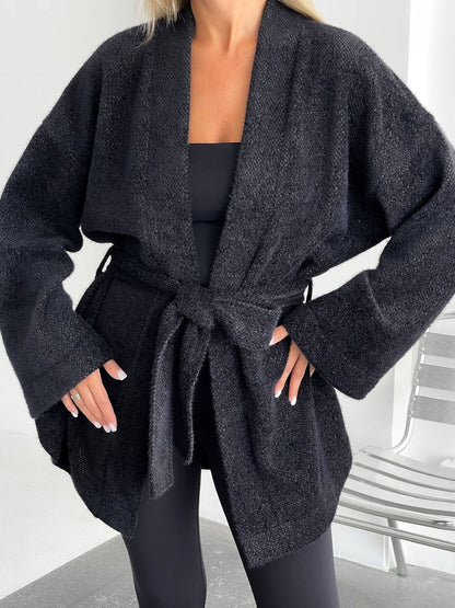 Person wearing a dark gray robe with a belt in a minimal indoor setting