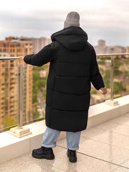 Person wearing a long black puffer coat on a rooftop with a cityscape view.