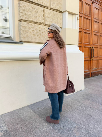 Woman in a long coat and hat standing on a street with a building in the background