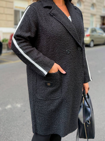 Person wearing a dark gray coat with white trim on a street.