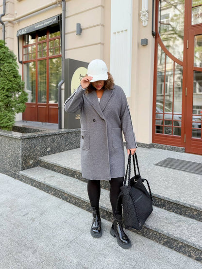 Person wearing a gray coat and black shoes standing on steps outside a building.