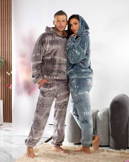 Two people wearing matching pajama sets with text design in a room.