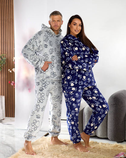 Two people wearing matching pajama sets with paw prints in a living room setting.