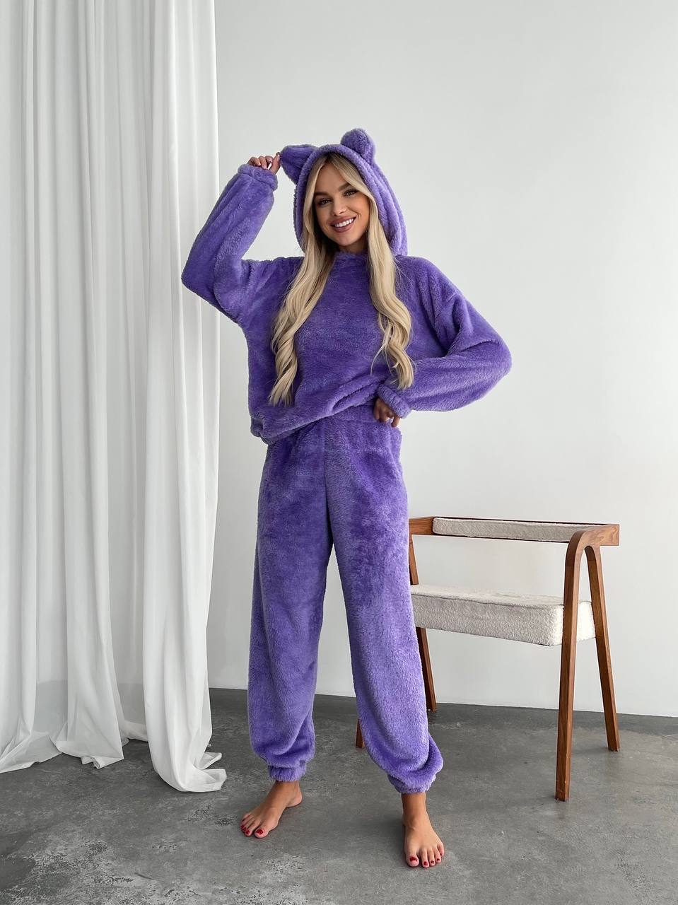 Person wearing a purple onesie with a hood in a minimalistic room.