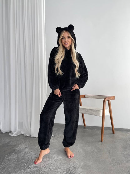 Person wearing a black onesie with bear ears in a minimalistic room.