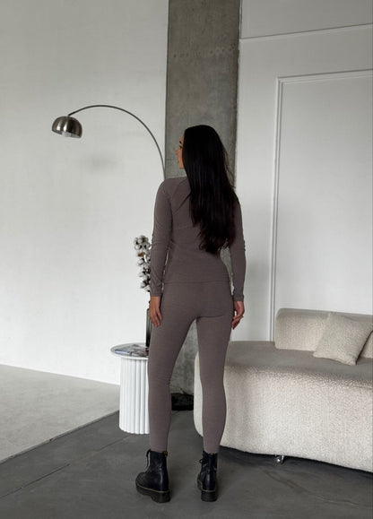 Woman in a gray jumpsuit standing in a modern living room.