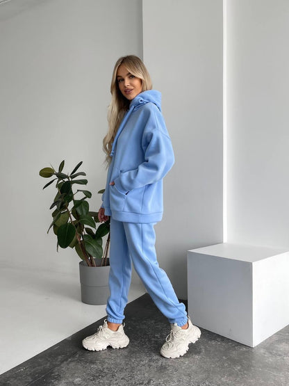 Person wearing a blue tracksuit standing in a minimalistic room with a plant and white cube.