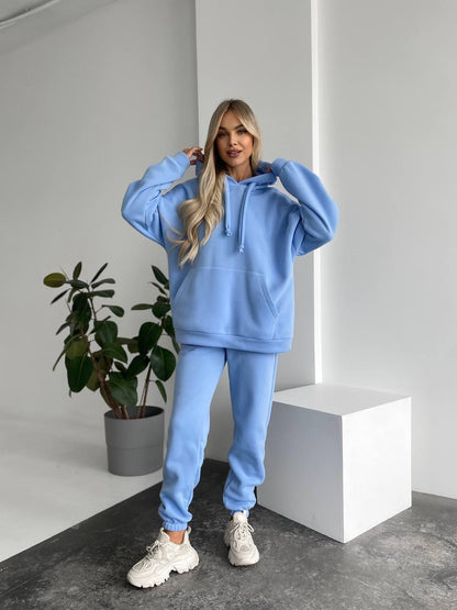 Woman wearing a blue hoodie and pants in a minimalistic room with a plant.