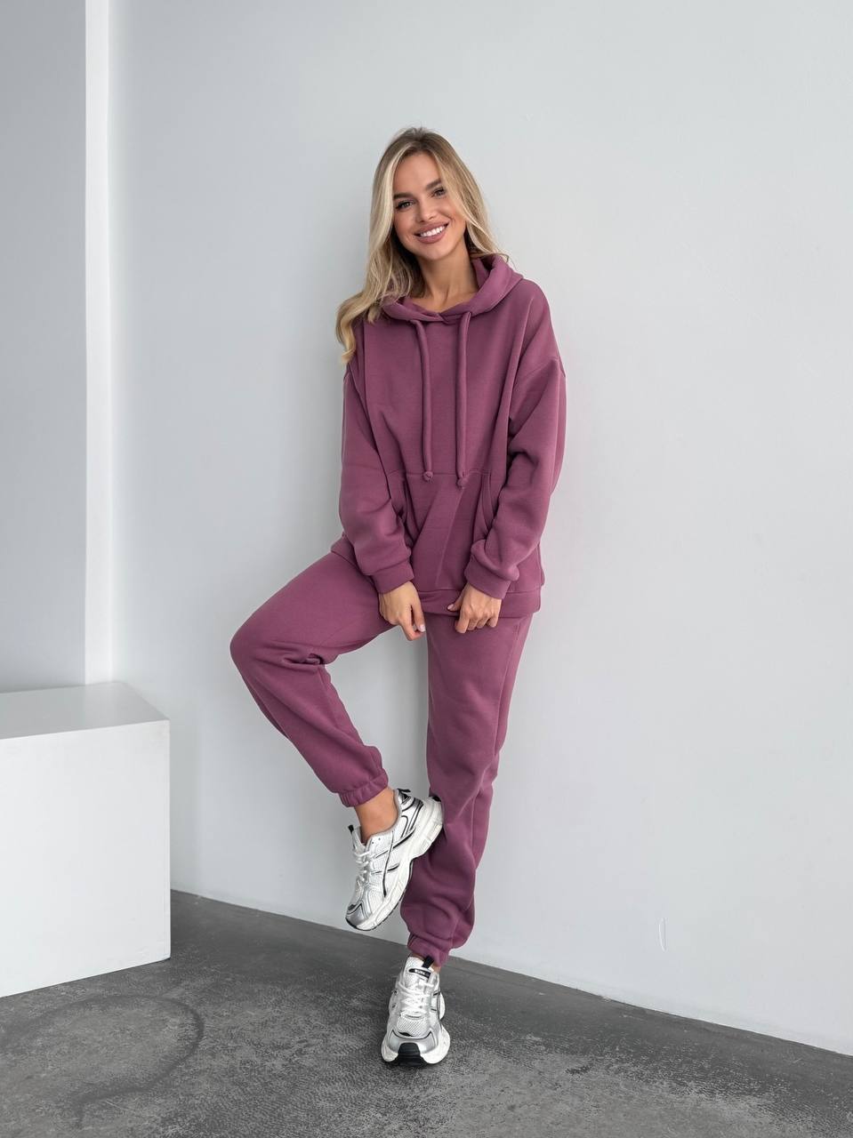 Woman wearing a purple tracksuit against a white wall