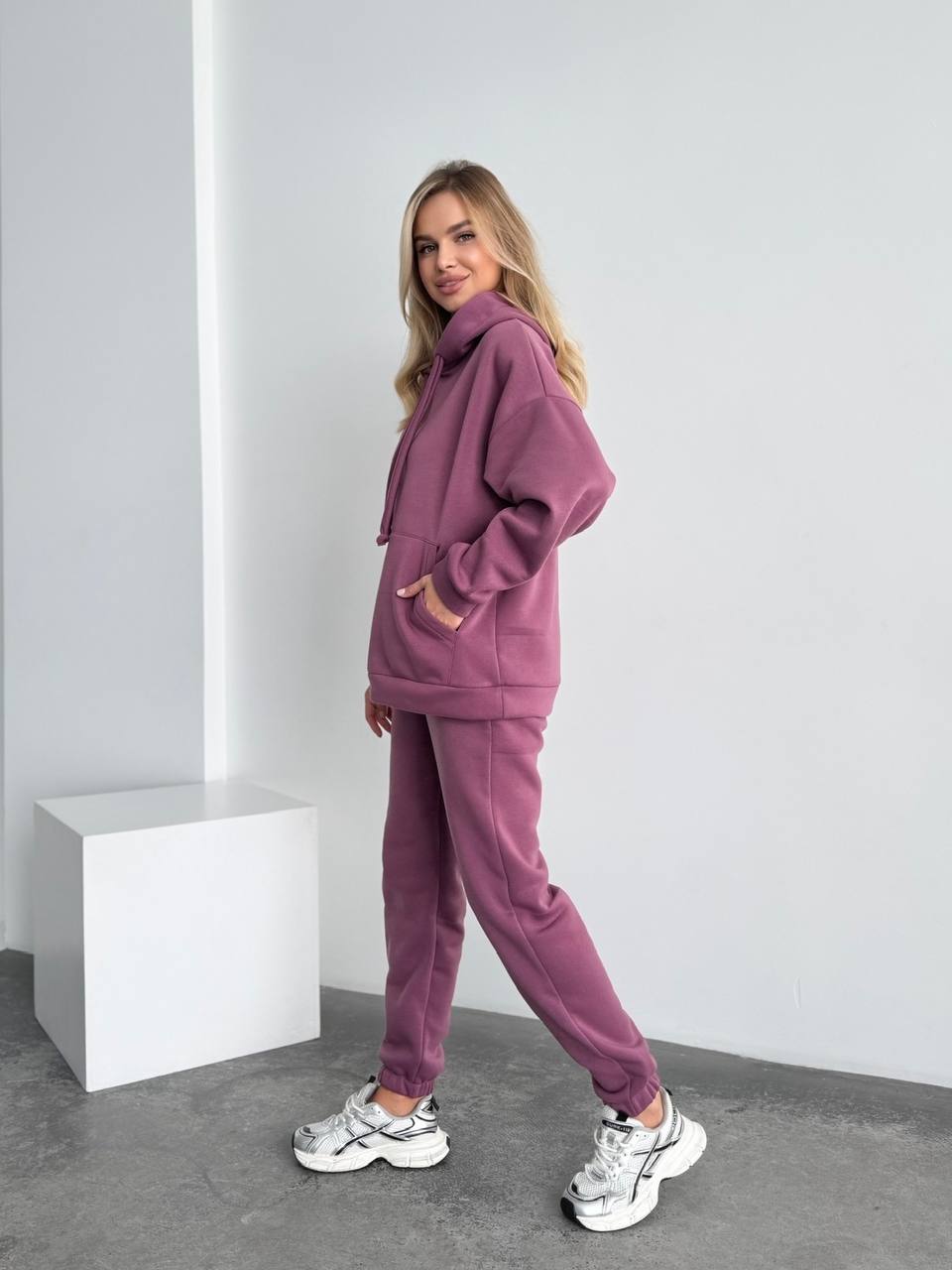 Woman wearing a purple tracksuit standing against a white background
