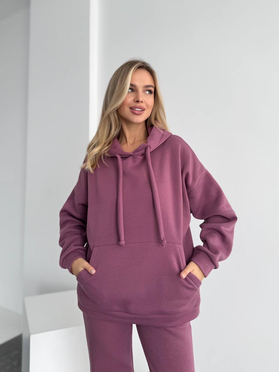 Woman wearing a purple hoodie and pants in a minimalistic setting