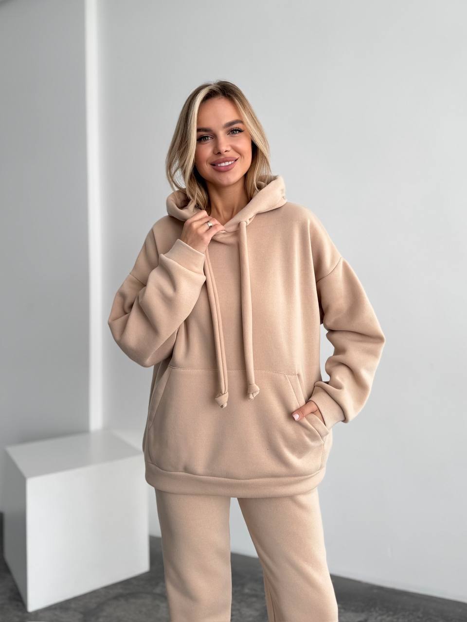 Woman wearing a beige hoodie and pants in a minimalistic setting