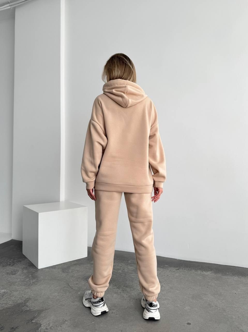 Person wearing a beige tracksuit standing in a minimalistic room.