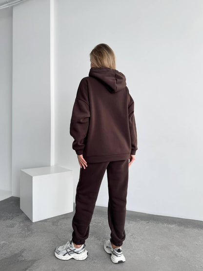 Person wearing a brown hoodie and pants in a minimalistic room.