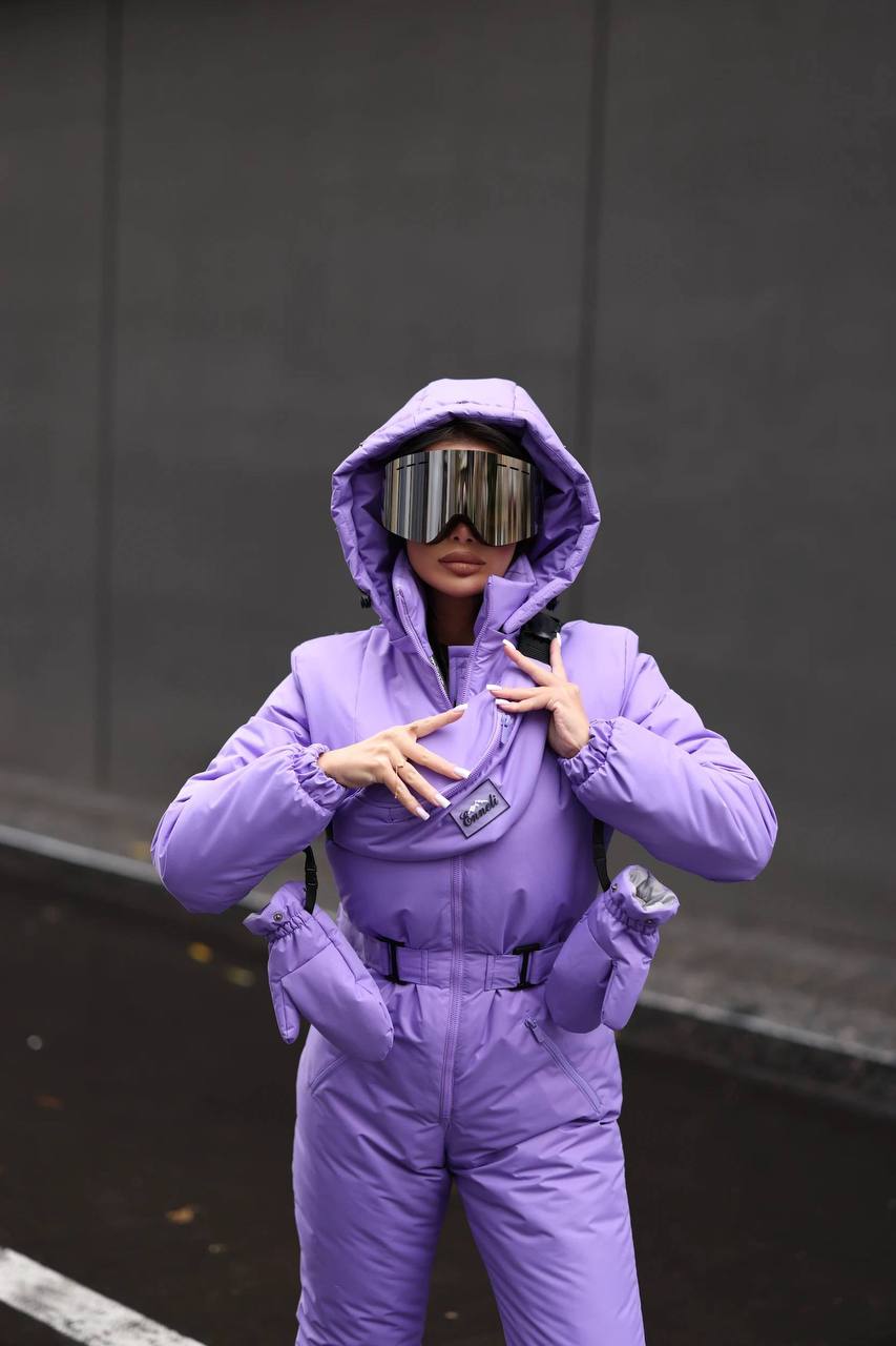 Person wearing a purple snowsuit with reflective goggles against a dark background