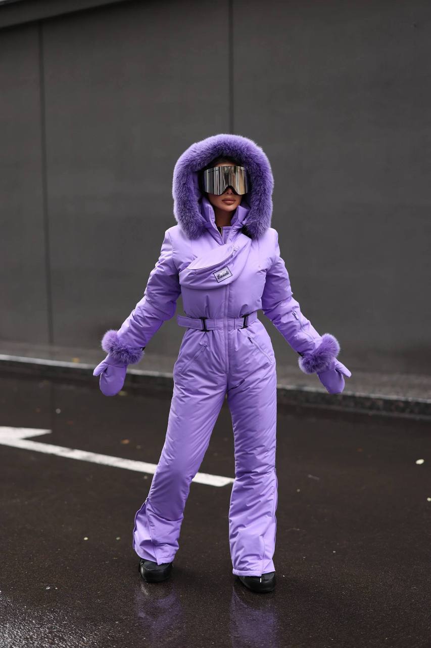 Person wearing a purple snowsuit with goggles on a dark surface.