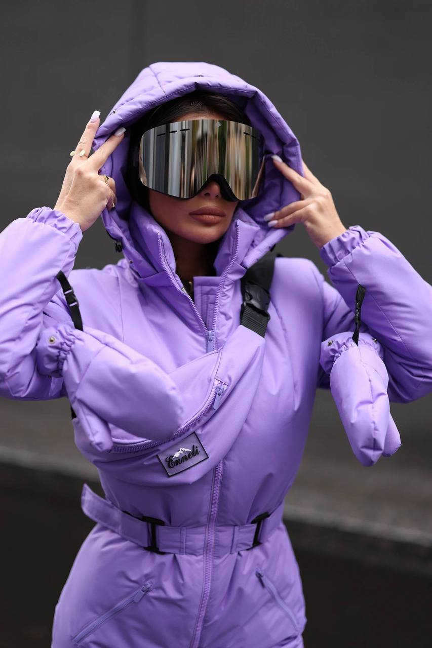 Person wearing a purple snowsuit with reflective goggles against a dark background