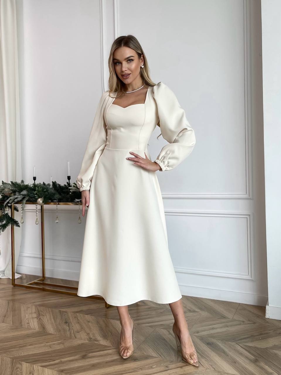 Woman in a white dress and matching jacket standing in a room with decorative elements.