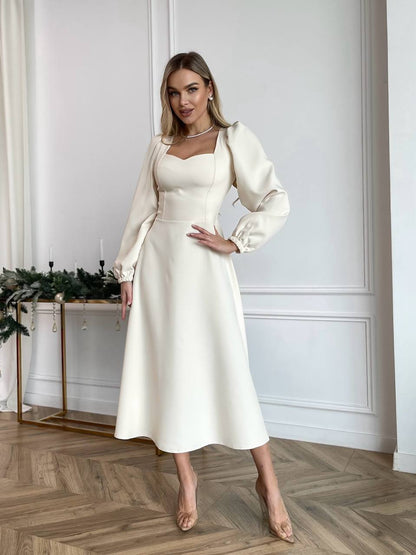 Woman in a white dress and matching jacket standing in a room with decorative elements.