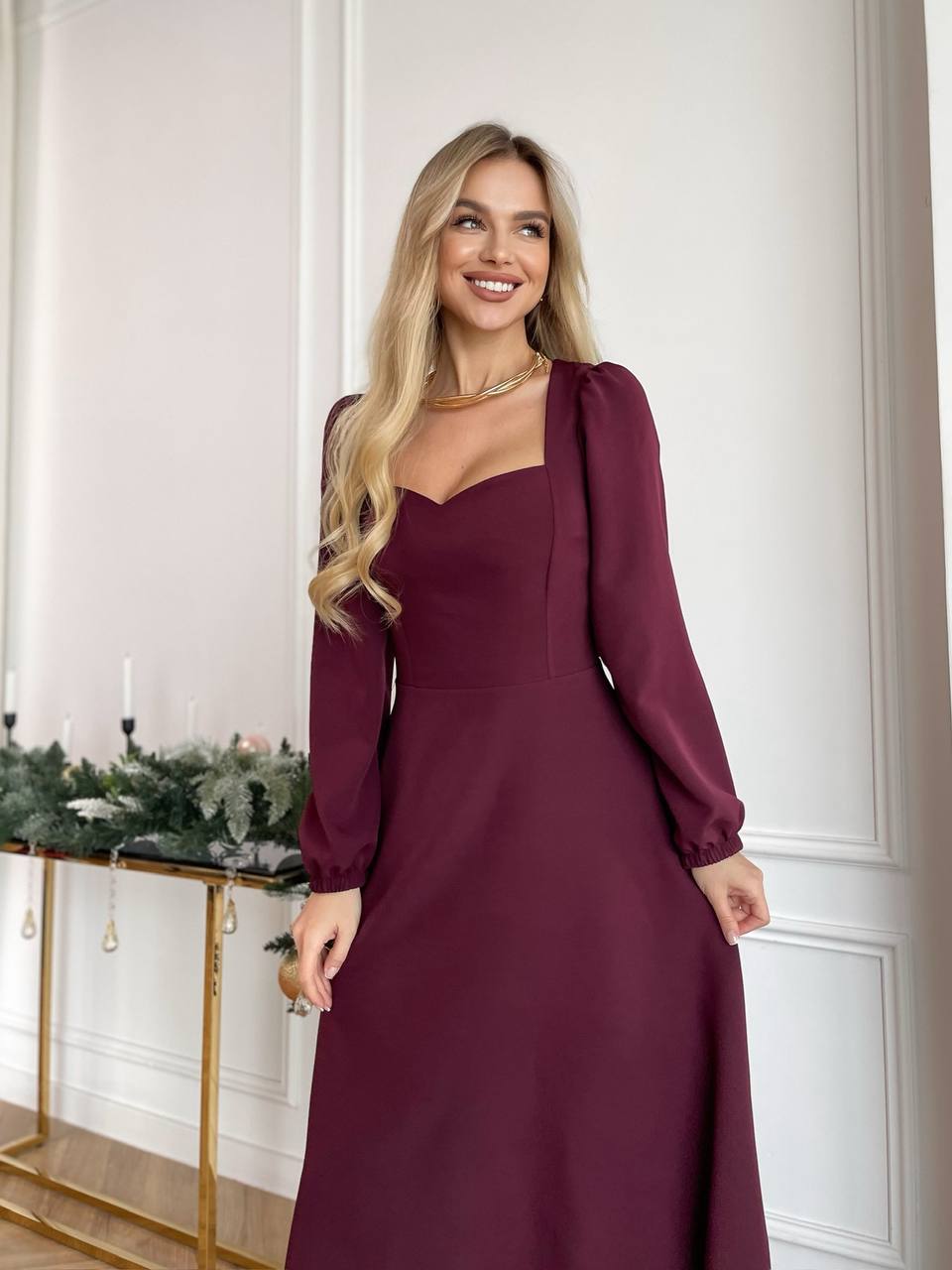 Woman wearing a burgundy dress standing in a room with decorative elements.