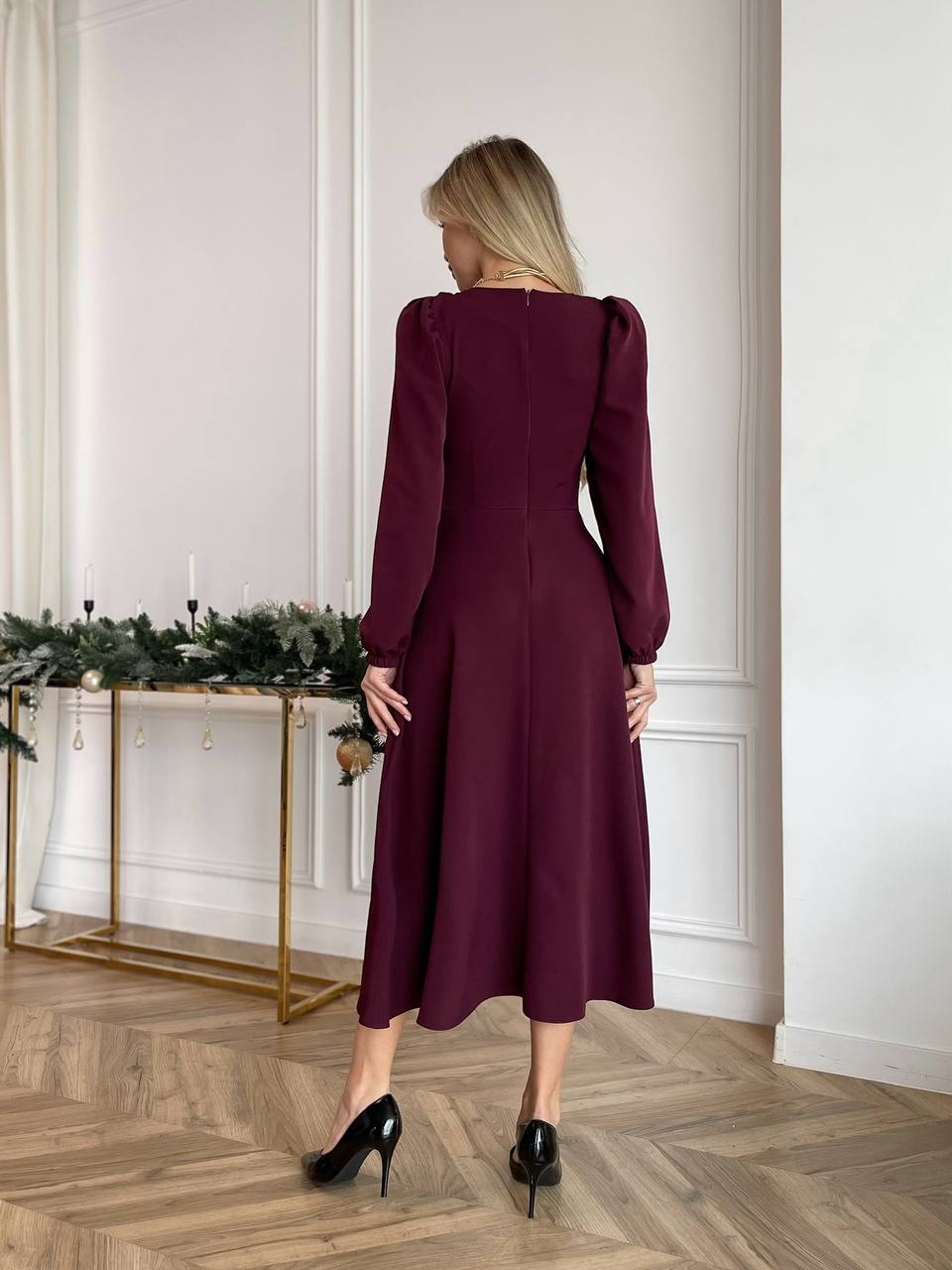 Woman in a burgundy dress standing in a room with decorative elements.