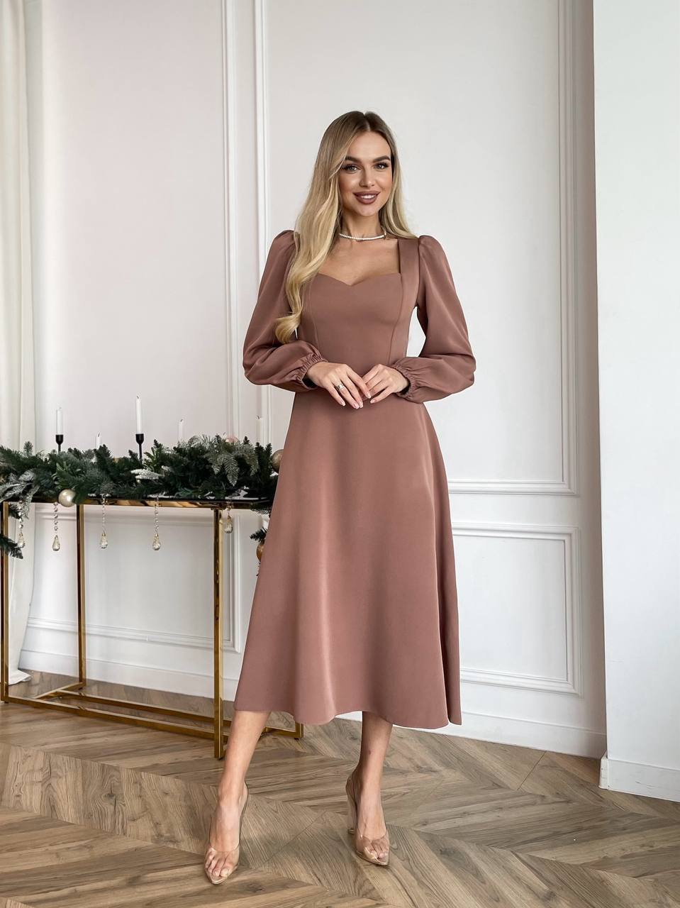 Woman in a brown dress standing in a room with decorative elements.