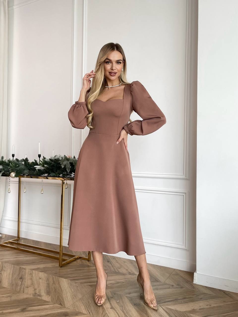 Woman wearing a brown dress in an elegant room with white walls and wooden floor.