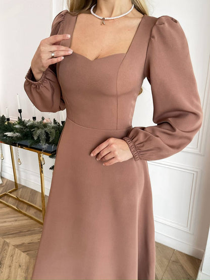 Woman wearing a brown dress with puffed sleeves in an indoor setting.
