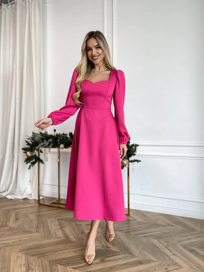 Woman in a pink dress standing in a room with white walls and wooden floor.