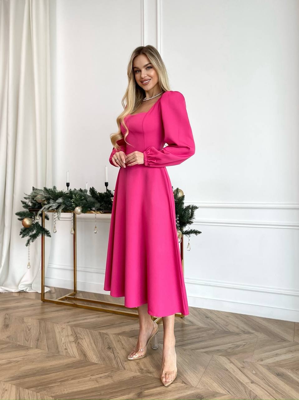 Woman in a pink dress standing in a room with decorative plants and a white wall.