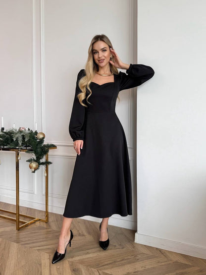 Woman in a black dress standing in a room with a decorative table and wall.