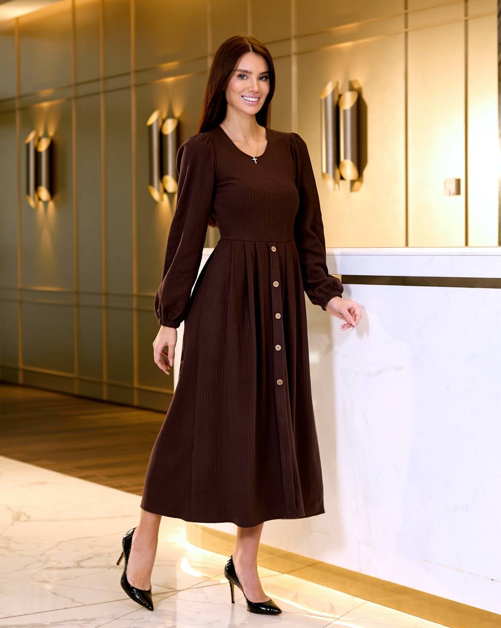 Woman in a brown dress standing in an elegant interior setting