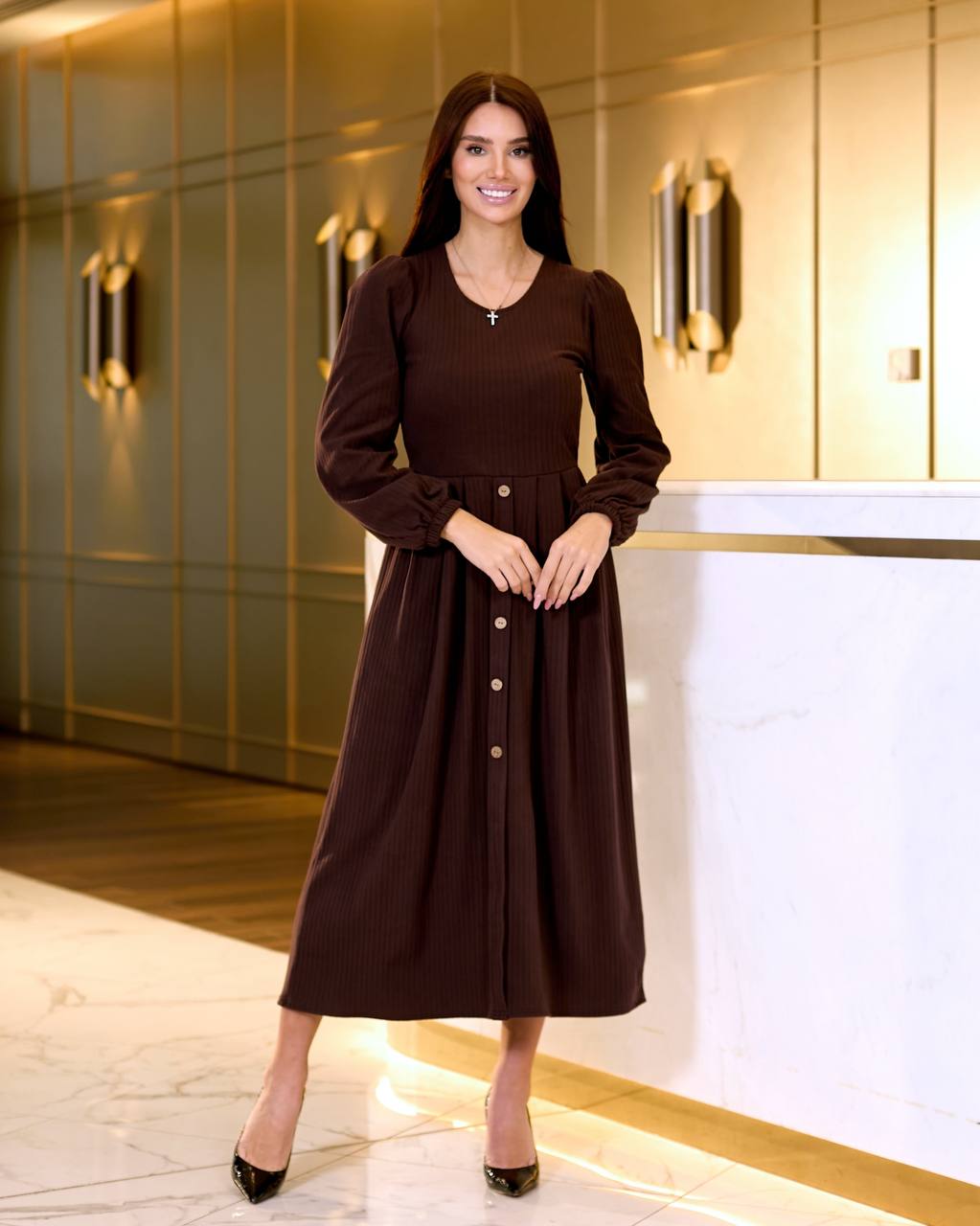 Woman in a brown dress standing in an elegant interior setting