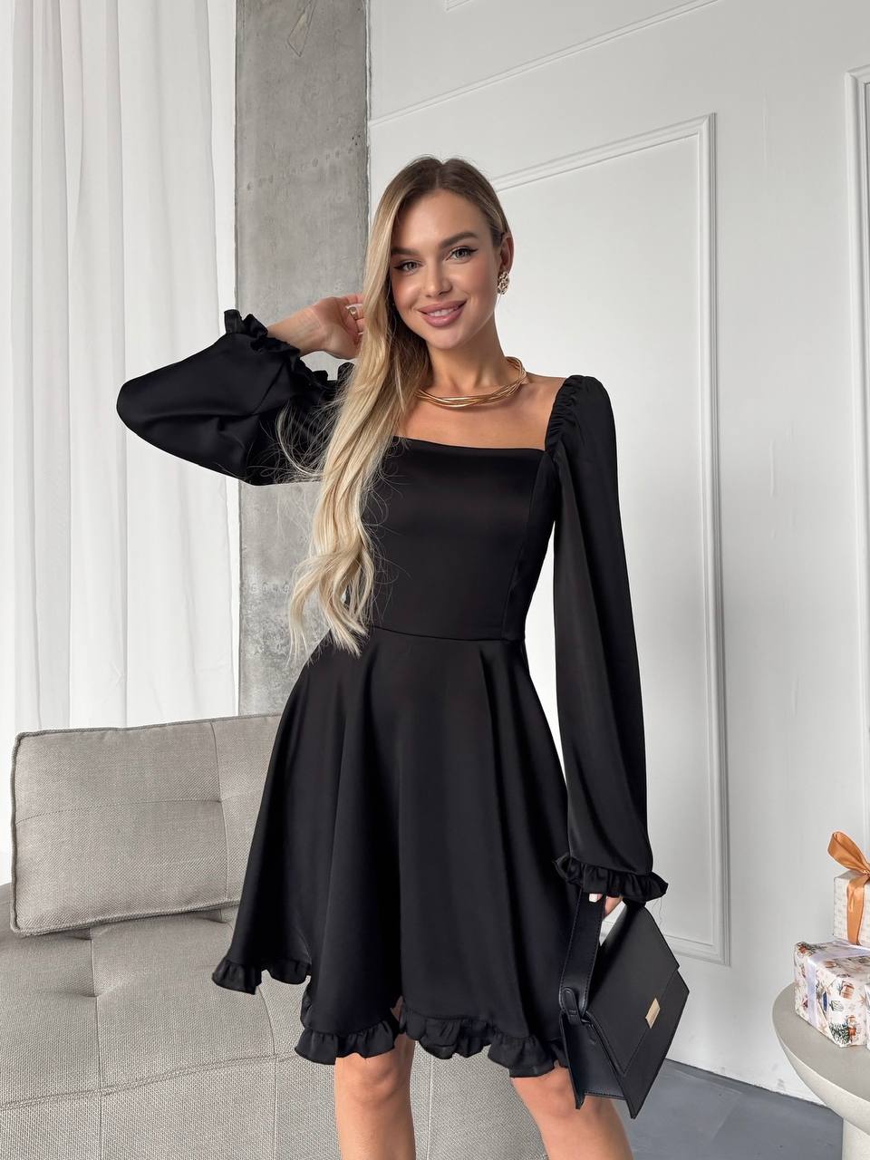 Woman wearing a black dress with long sleeves in an indoor setting.