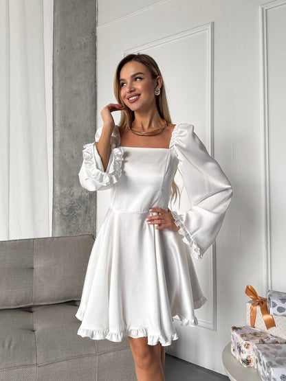 Woman wearing a white dress with ruffled sleeves in a room.