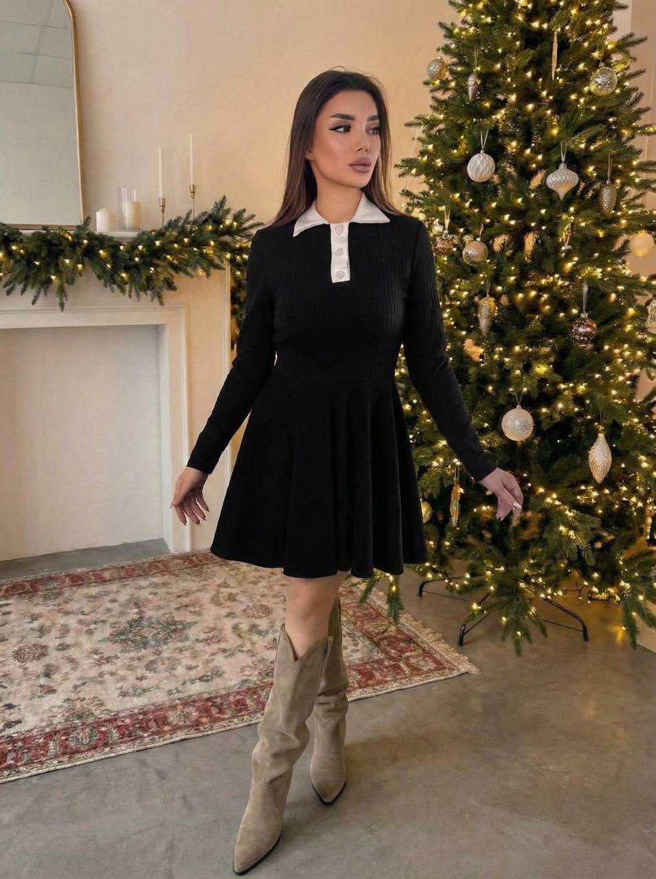 Woman in a black dress with a white collar standing in front of a decorated Christmas tree.