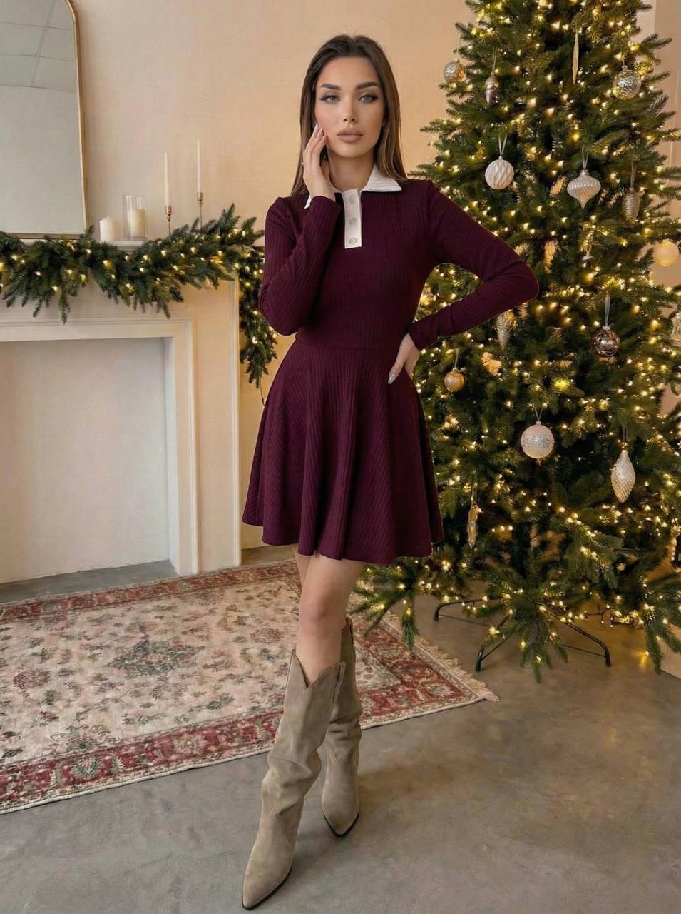 Woman in a burgundy dress with a white collar standing in front of a decorated Christmas tree.