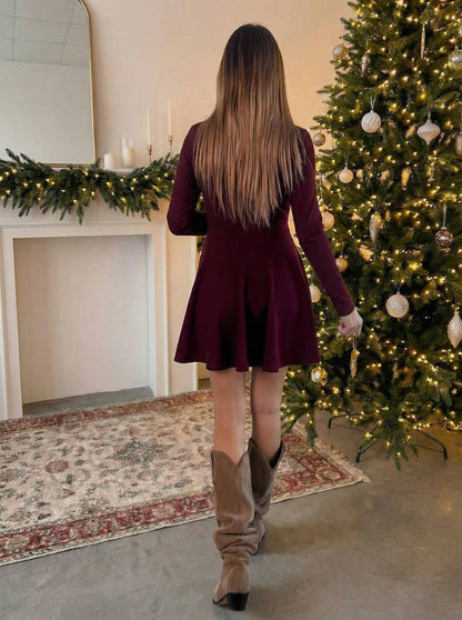 Woman in a burgundy dress and brown boots walking towards a decorated Christmas tree.