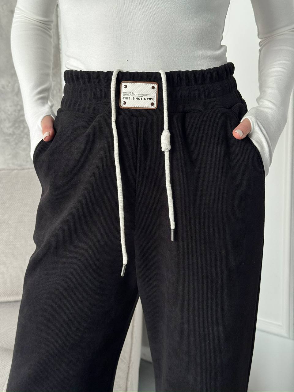 Black pants with a visible brand label worn by a person against a neutral background