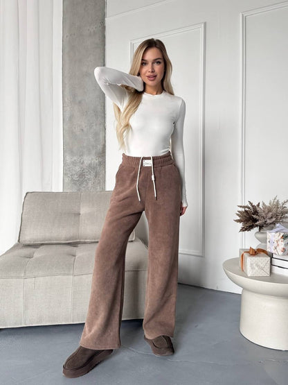 Woman wearing a white top and brown pants in a modern room.