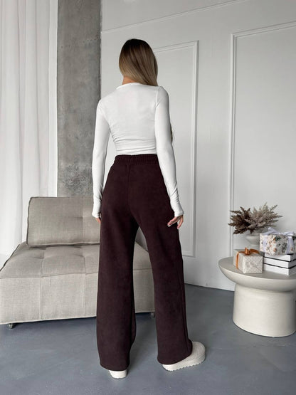 Person wearing a white long-sleeve top and brown pants in a modern living room.