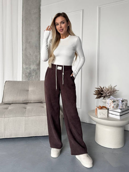 Woman in a white top and brown pants standing in a modern living room.