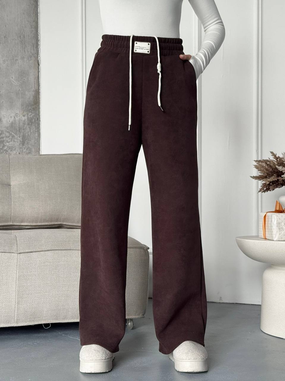 Person wearing brown wide-leg pants with a white top in a minimalistic room.