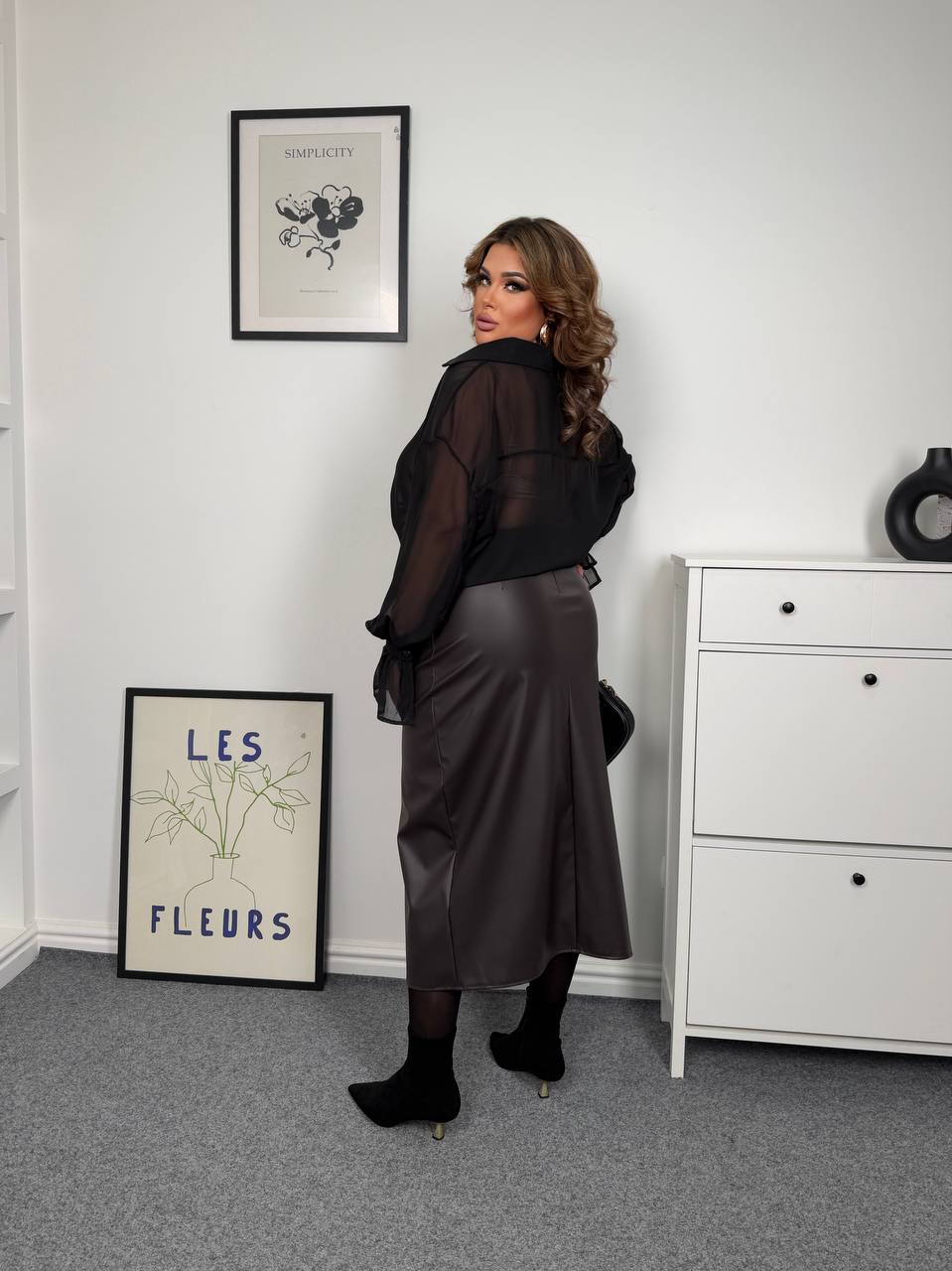 Woman in a dark outfit standing in a room with white walls and furniture.